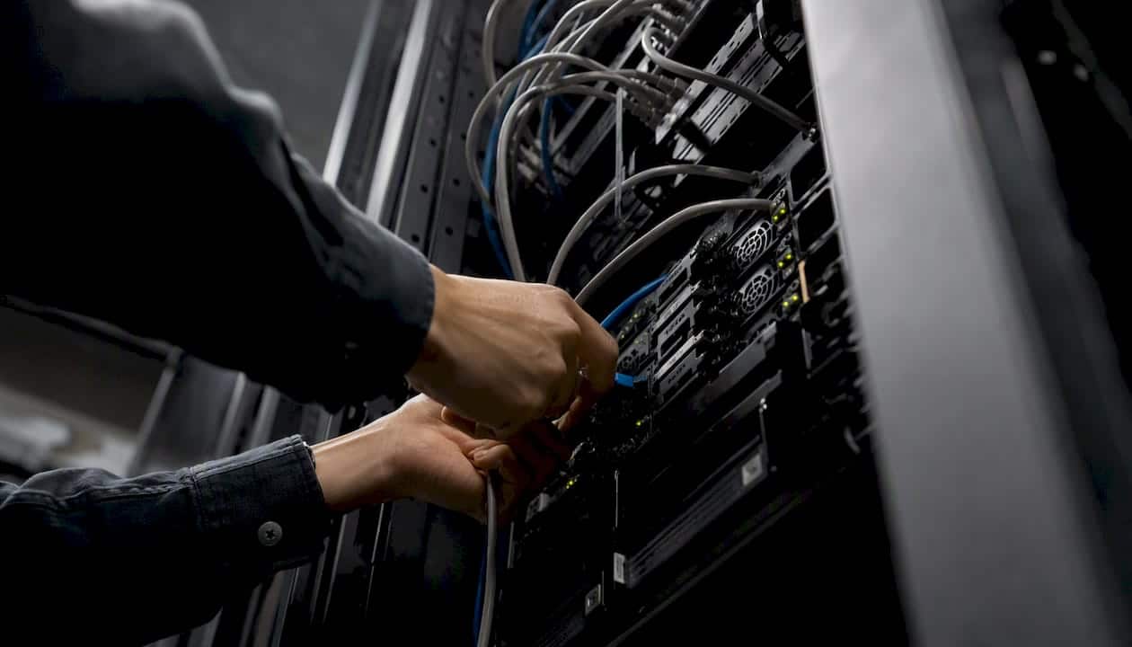 Des mains connectent un câble réseau à une baie de serveurs.